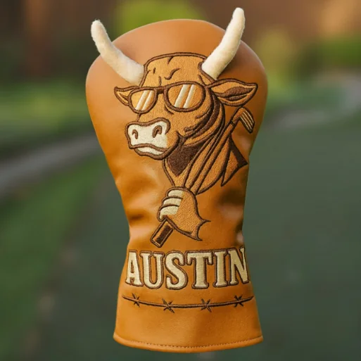 A tan driver headcover with horns, embroidered with a longhorn in sunglasses holding a club above the word AUSTIN