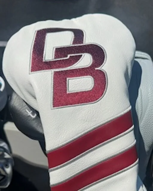 A white driver headcover embroidered with a maroon DB monogram above two maroon stripes